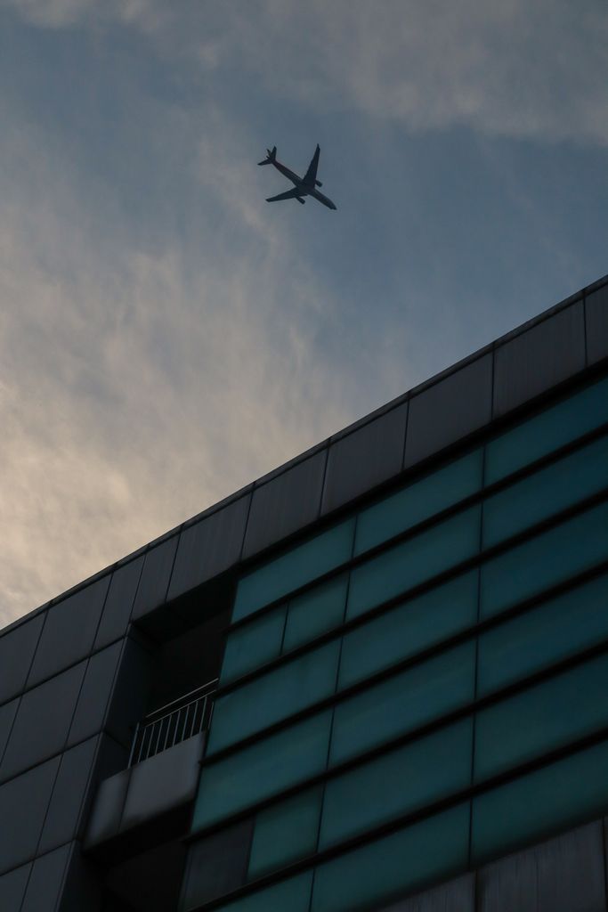 A plane flying over a modern building against a cloudy sky, showcasing urban architecture.