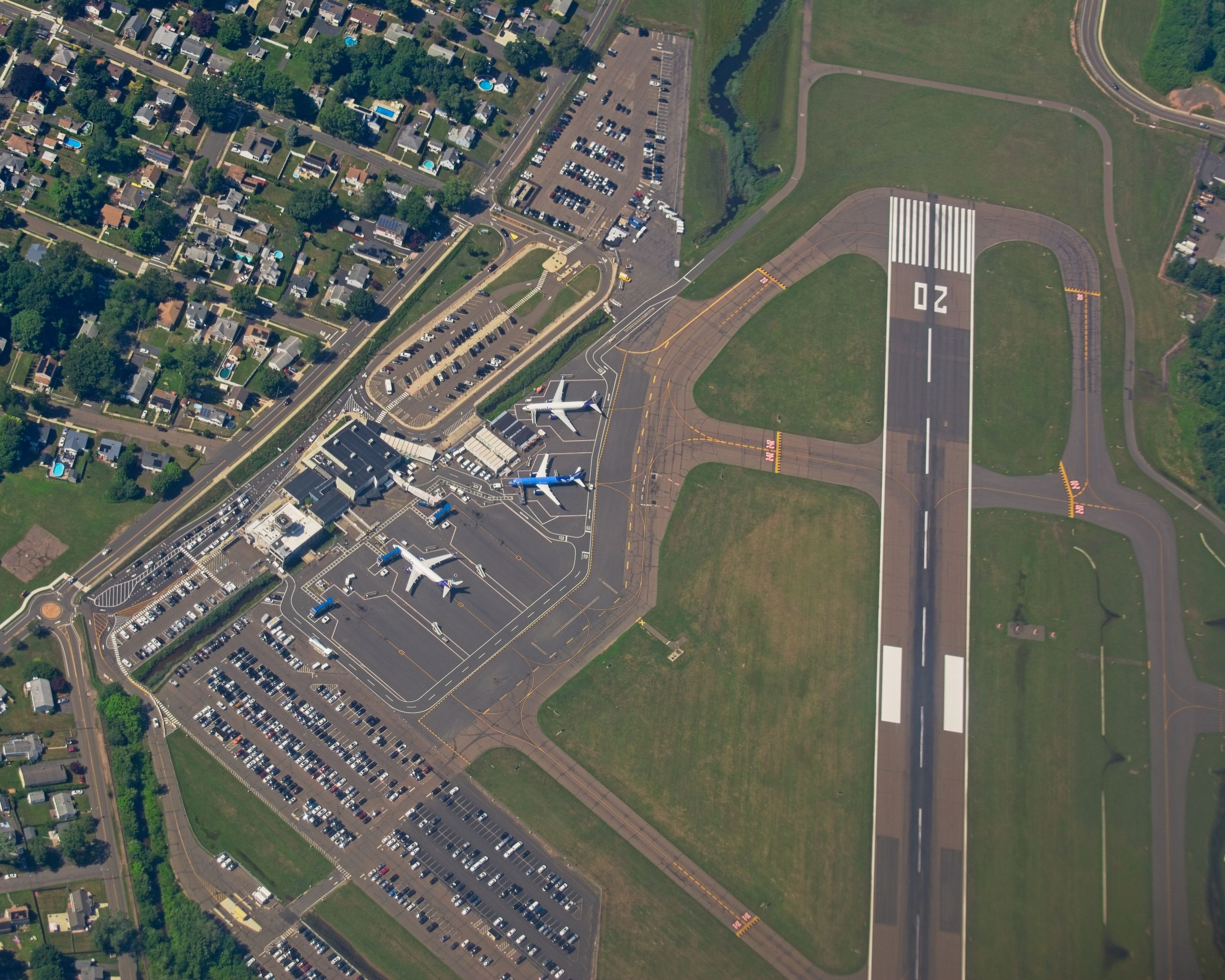 Aerial shot of an airport in New York, showcasing runways, planes, and nearby neighborhoods.