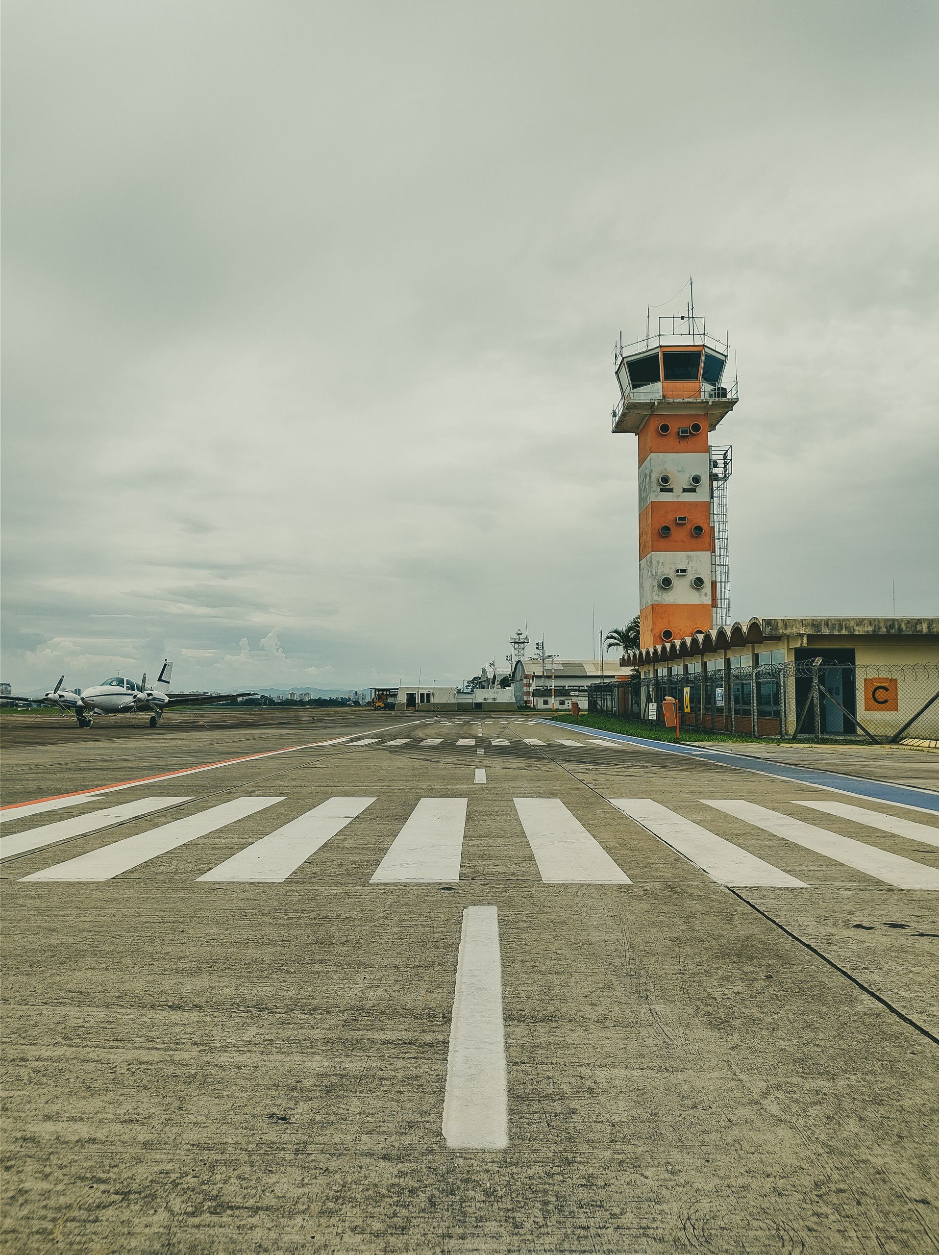 Vertical shot of an airport runway with a control tower and airplane, under a cloudy sky.